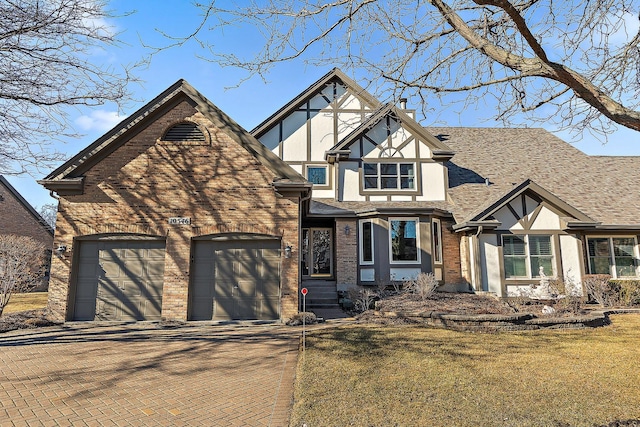 english style home with a garage, brick siding, roof with shingles, decorative driveway, and stucco siding