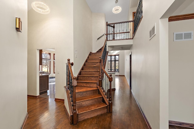 stairs featuring a high ceiling, wood finished floors, visible vents, and baseboards