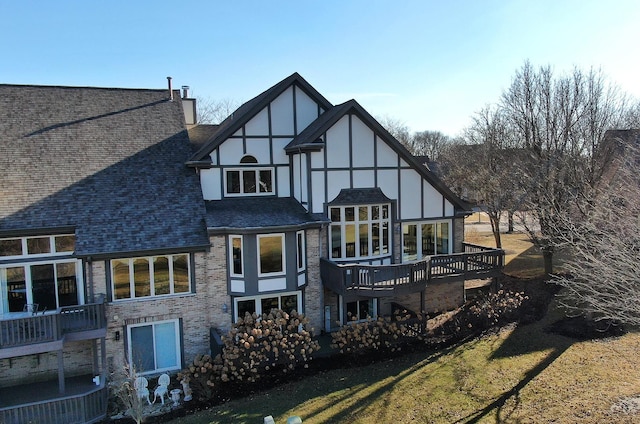 back of house with stucco siding, a chimney, and roof with shingles