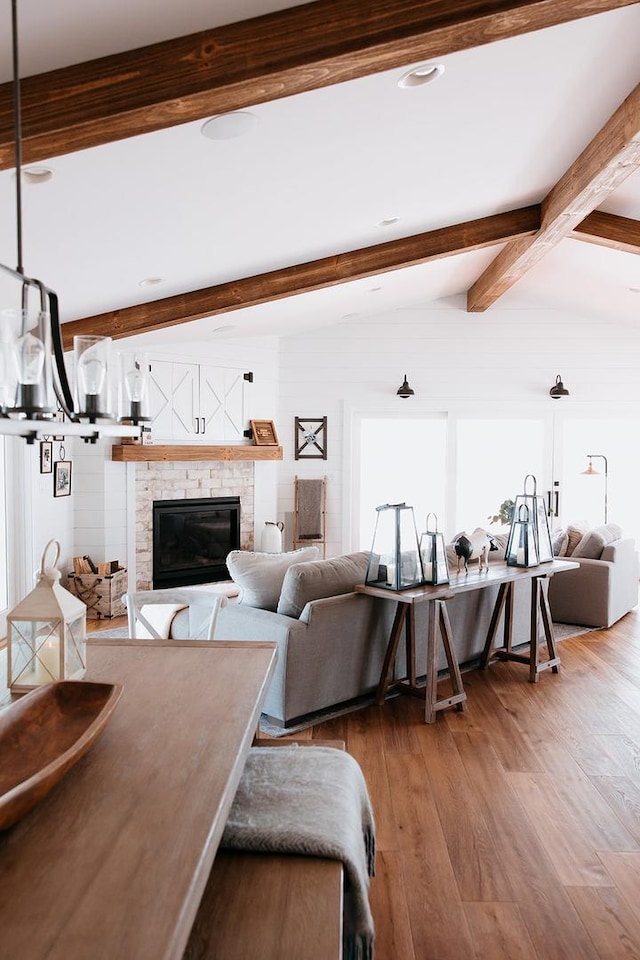 living area featuring lofted ceiling with beams, wood finished floors, and a glass covered fireplace