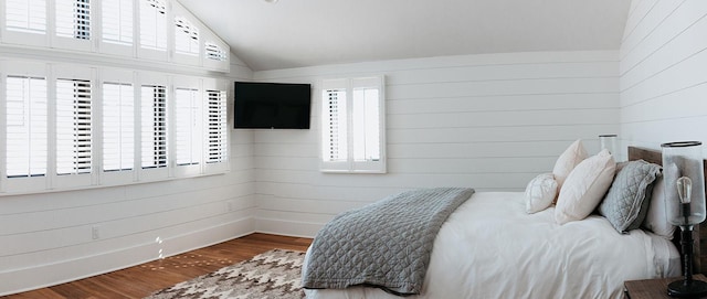 bedroom featuring vaulted ceiling, wood walls, and wood finished floors