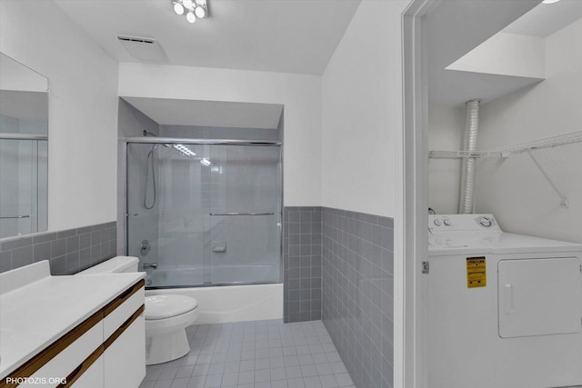 bathroom with toilet, vanity, tile walls, tile patterned floors, and washer / dryer