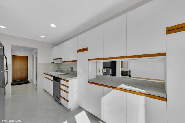 kitchen featuring light tile patterned floors, light countertops, stainless steel dishwasher, white cabinetry, and a sink