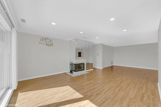 unfurnished living room featuring light wood-style flooring, recessed lighting, a multi sided fireplace, visible vents, and baseboards