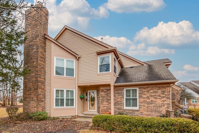 view of front facade with a shingled roof, central AC unit, and brick siding