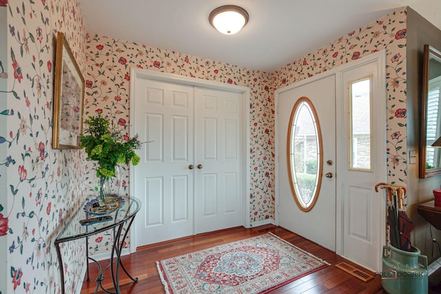 foyer entrance with wallpapered walls, visible vents, and hardwood / wood-style floors