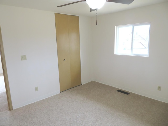 spare room with light carpet, ceiling fan, visible vents, and baseboards