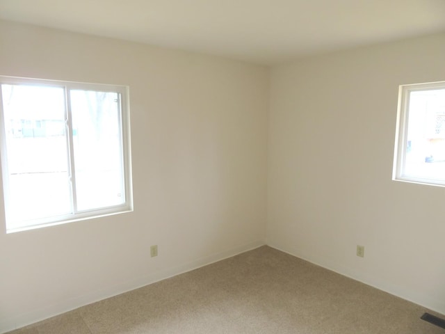 empty room featuring plenty of natural light, carpet flooring, and visible vents