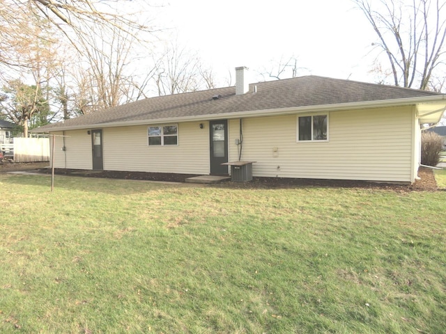 back of house featuring roof with shingles, a lawn, and a chimney