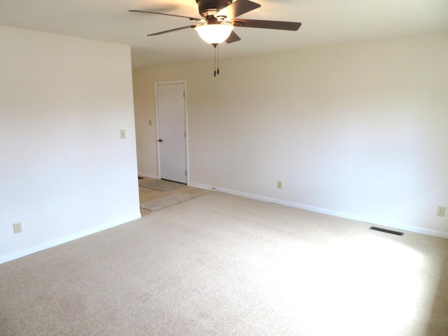 spare room with a ceiling fan, light colored carpet, visible vents, and baseboards