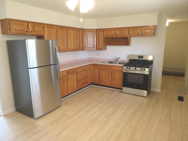 kitchen featuring light countertops, appliances with stainless steel finishes, brown cabinetry, a sink, and light wood-type flooring