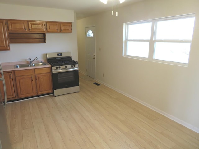 kitchen with brown cabinets, visible vents, light wood-style floors, stainless steel gas range oven, and baseboards