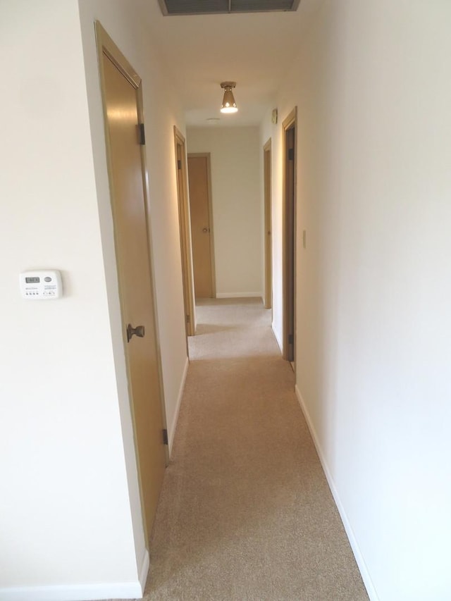 corridor with baseboards, visible vents, and light colored carpet