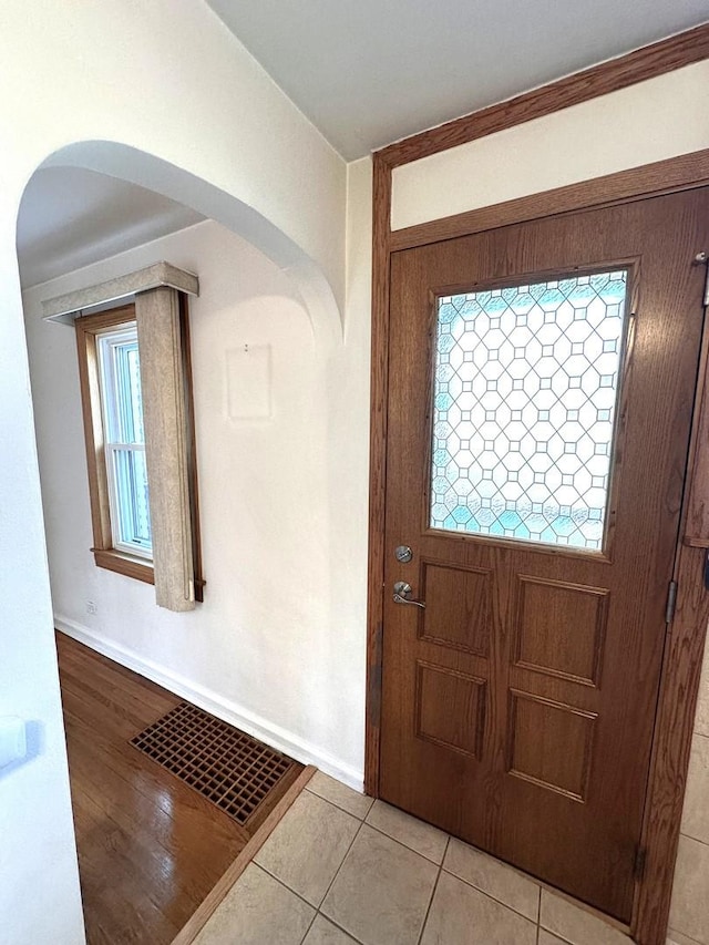 foyer featuring light tile patterned floors, baseboards, visible vents, and arched walkways