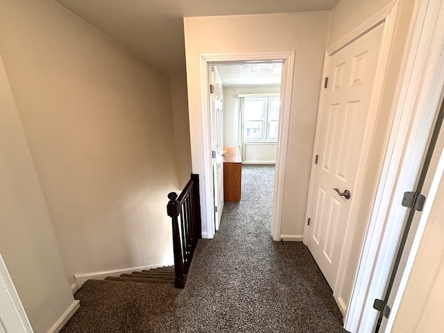 corridor featuring dark carpet, an upstairs landing, and baseboards