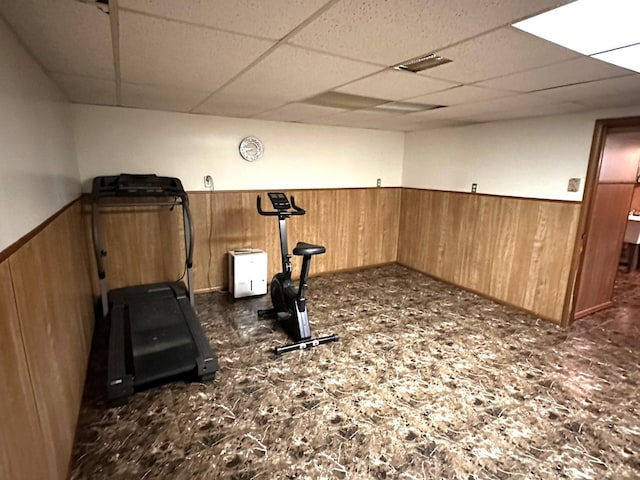 workout area featuring wooden walls, a drop ceiling, and wainscoting