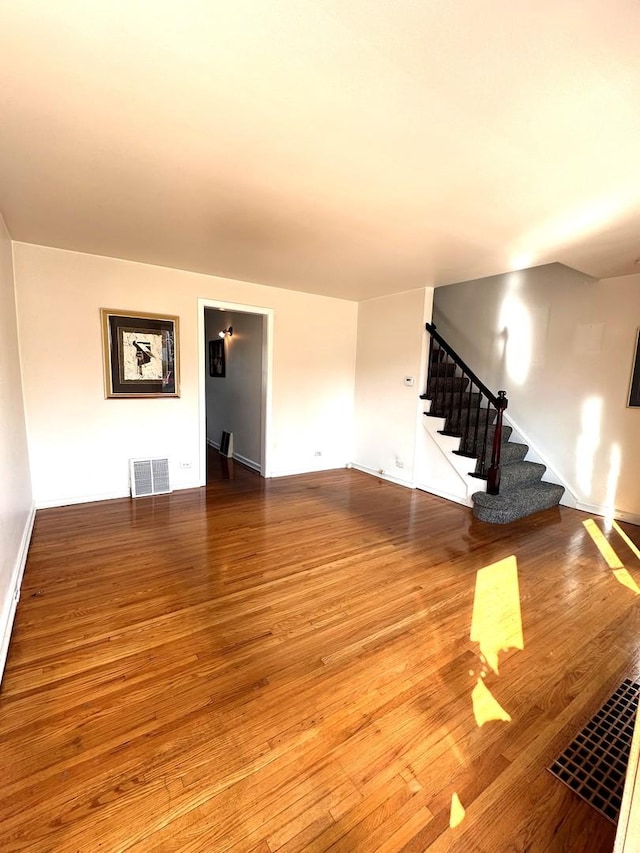 unfurnished living room with visible vents, stairway, and wood finished floors