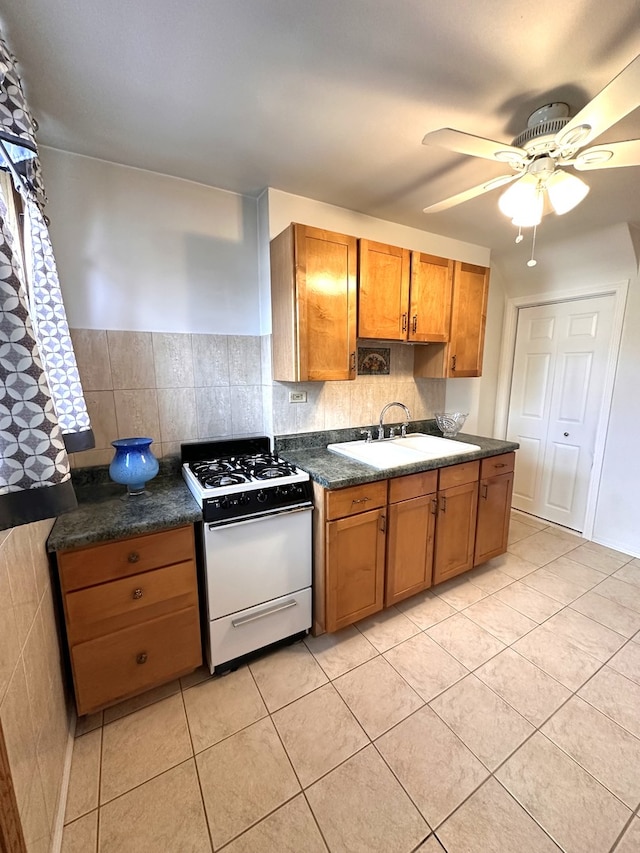 kitchen with light tile patterned floors, brown cabinetry, dark countertops, white gas stove, and a sink