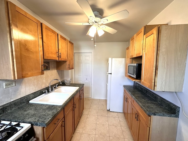 kitchen with decorative backsplash, dark countertops, stainless steel microwave, freestanding refrigerator, and a sink