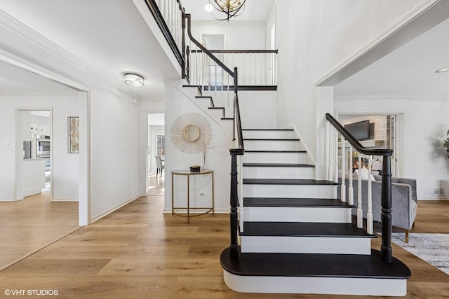 foyer entrance with baseboards, wood finished floors, stairs, a high ceiling, and crown molding