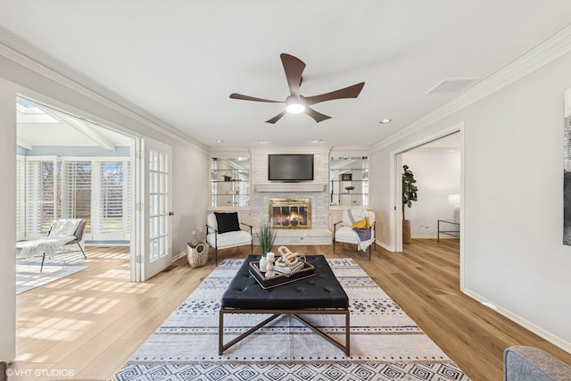 living room with a brick fireplace, baseboards, crown molding, and light wood finished floors