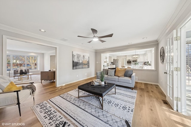 living room featuring baseboards, light wood finished floors, visible vents, and crown molding