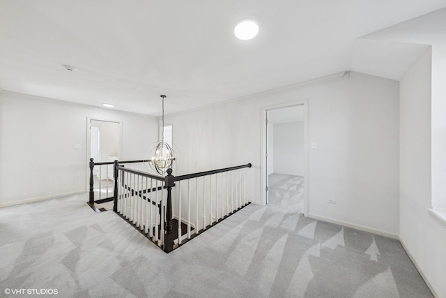 corridor featuring a chandelier, carpet flooring, an upstairs landing, and baseboards