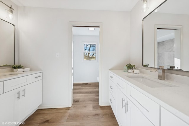 bathroom featuring baseboards, toilet, wood finished floors, a sink, and two vanities