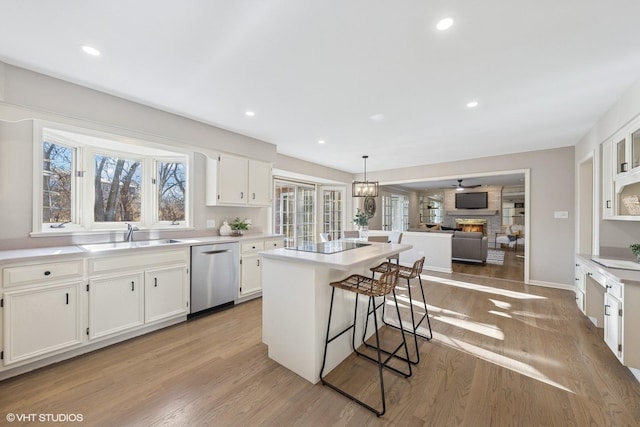 kitchen with a kitchen island, a sink, white cabinets, stainless steel dishwasher, and light wood finished floors