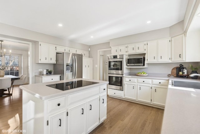 kitchen with light wood finished floors, a kitchen island, stainless steel appliances, light countertops, and a sink