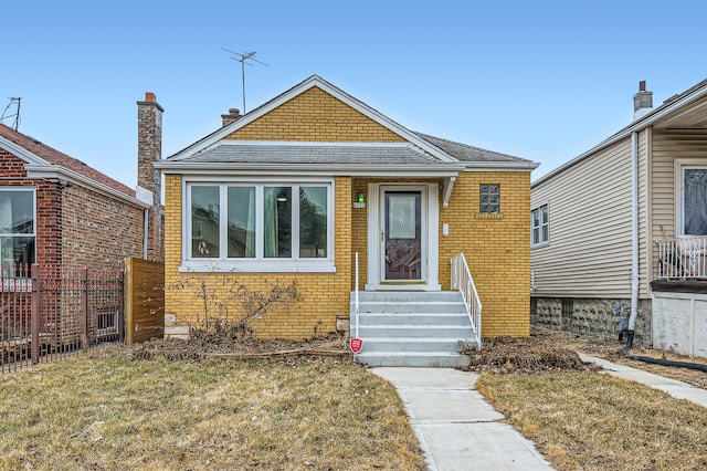 bungalow-style home with a shingled roof, a front yard, fence, and brick siding