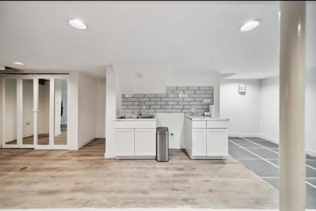 kitchen with light wood finished floors, tasteful backsplash, white cabinets, light countertops, and a sink