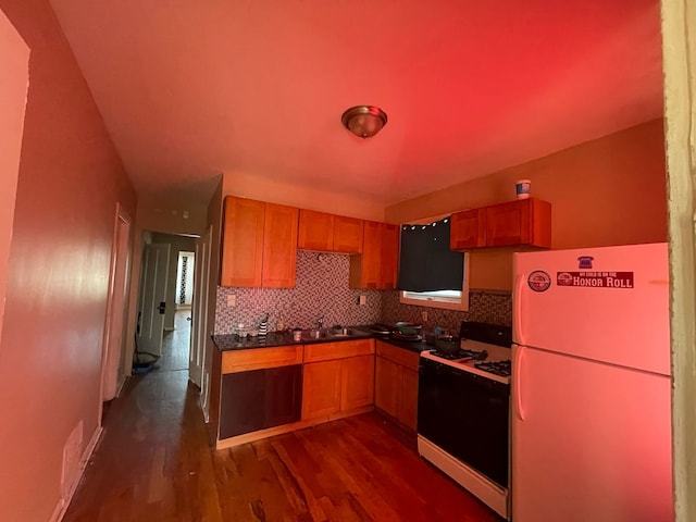 kitchen with dark wood-style flooring, freestanding refrigerator, decorative backsplash, dark countertops, and gas range