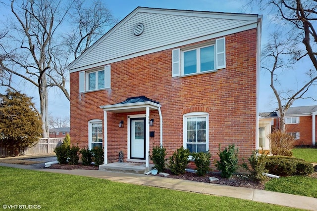 colonial house featuring brick siding, a front yard, and fence