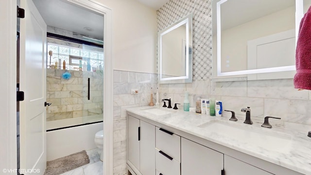 full bath with double vanity, a sink, toilet, and tile walls