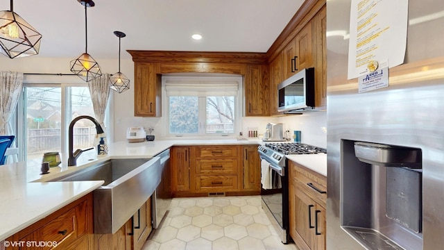 kitchen with stainless steel appliances, light countertops, brown cabinetry, and decorative light fixtures