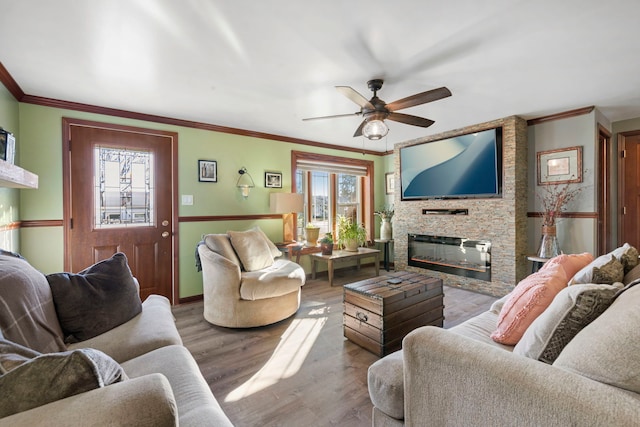 living room featuring a fireplace, wood finished floors, a ceiling fan, baseboards, and ornamental molding