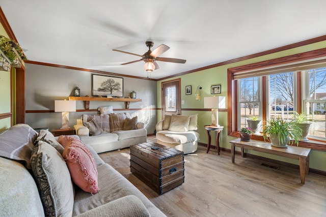 living area with light wood-style floors, a ceiling fan, baseboards, and crown molding