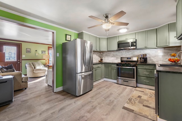 kitchen with green cabinetry, dark countertops, appliances with stainless steel finishes, ornamental molding, and a sink