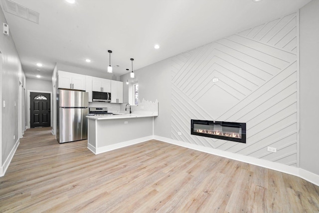 kitchen with stainless steel appliances, backsplash, light wood-style floors, visible vents, and a peninsula
