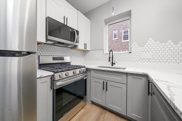 kitchen featuring gray cabinets, backsplash, a sink, and stainless steel appliances