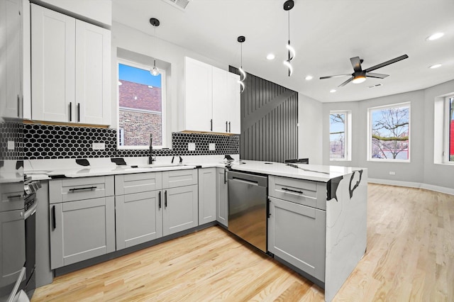 kitchen with stainless steel dishwasher, backsplash, a sink, a ceiling fan, and a peninsula