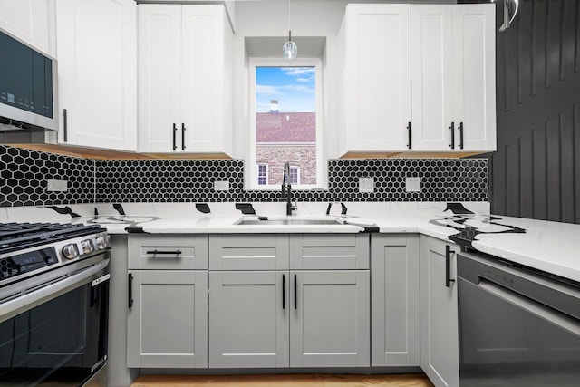 kitchen with decorative backsplash, stainless steel appliances, a sink, light stone counters, and pendant lighting