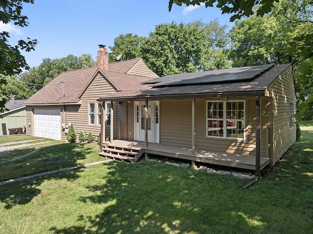 view of front of home featuring a chimney, an attached garage, covered porch, roof mounted solar panels, and a front yard