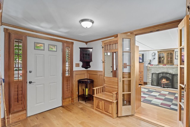 foyer entrance featuring a wainscoted wall, a lit fireplace, light wood finished floors, and crown molding