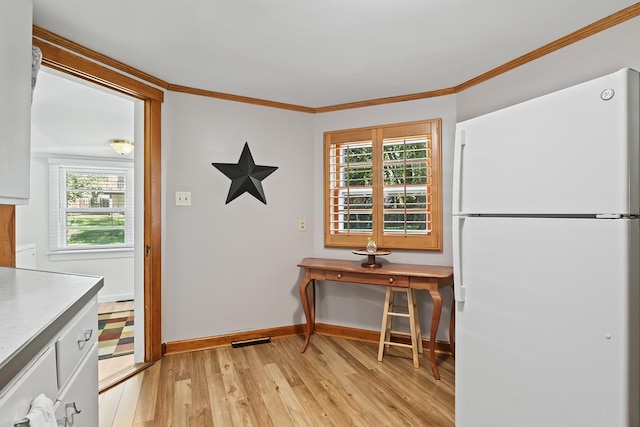 kitchen featuring light wood finished floors, baseboards, visible vents, ornamental molding, and freestanding refrigerator