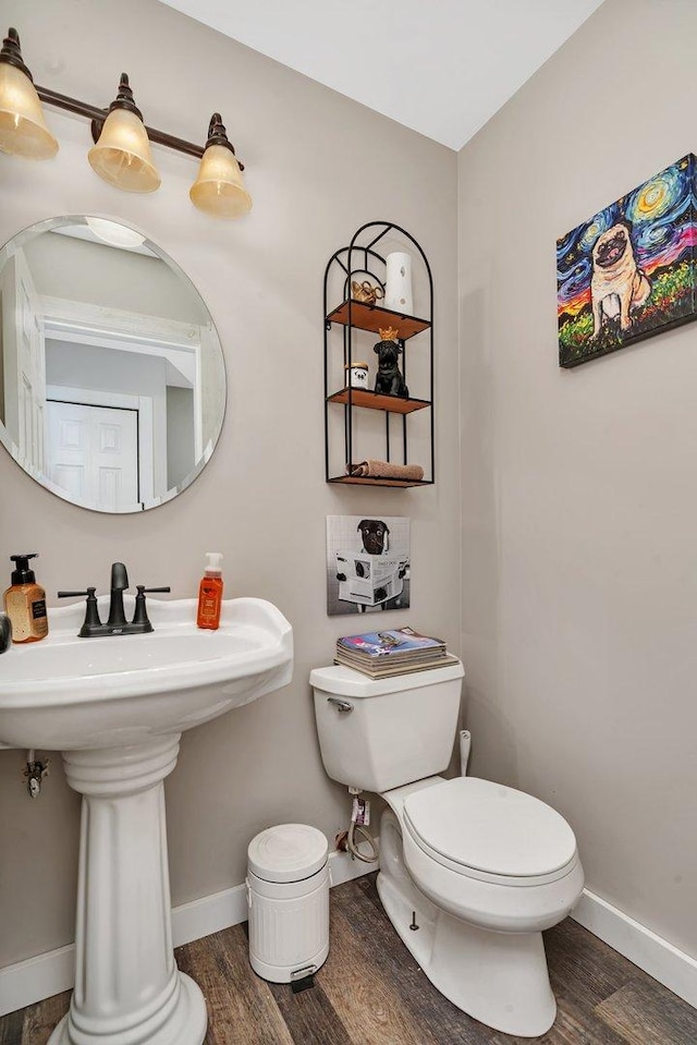 half bathroom featuring baseboards, a sink, toilet, and wood finished floors