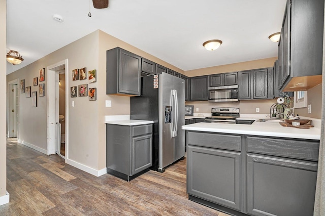 kitchen with gray cabinets, light countertops, appliances with stainless steel finishes, wood finished floors, and a peninsula