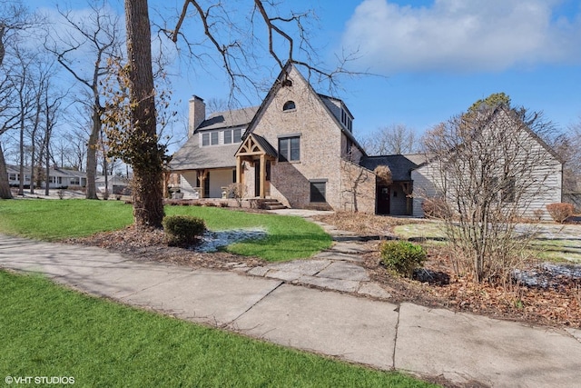 tudor-style house with brick siding, a chimney, and a front yard