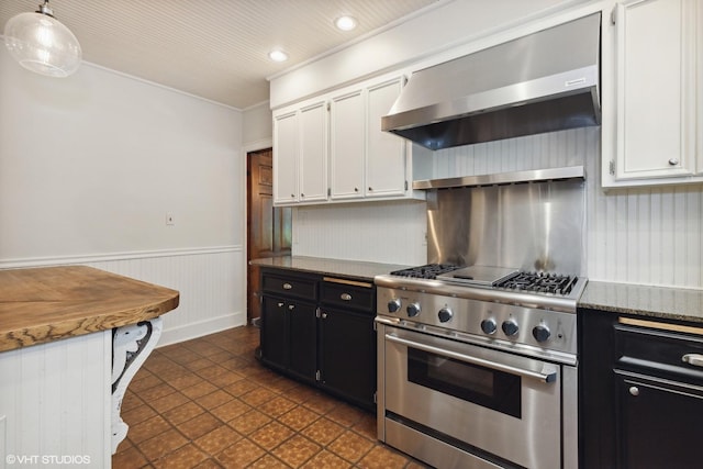 kitchen featuring white cabinets, dark cabinetry, wainscoting, wall chimney exhaust hood, and stainless steel range